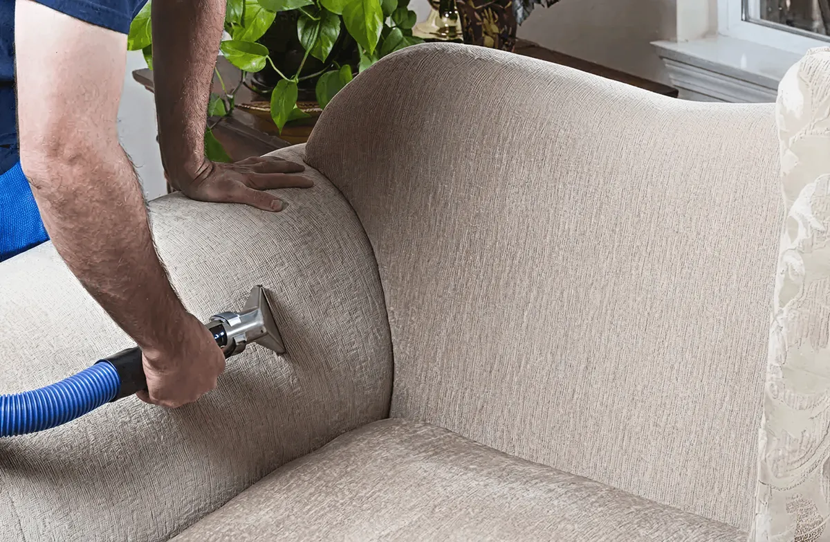 Professional upholstery cleaner deep-cleaning a fabric sofa with a handheld extraction tool and hose, San Francisco, CA.